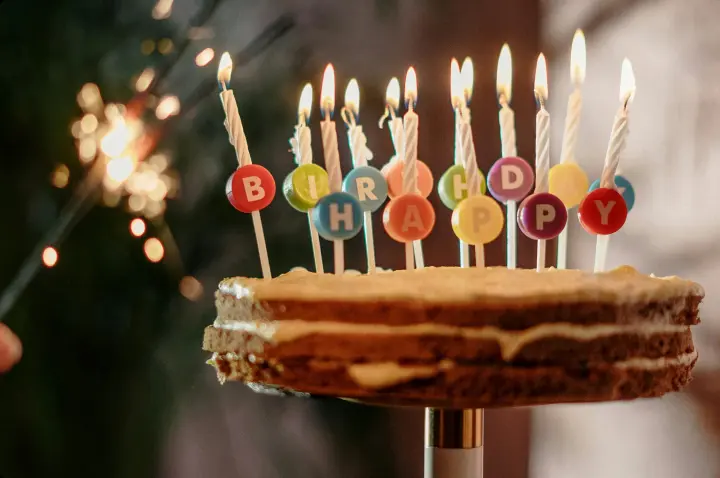 Three-layer Birthday Cake with lit candles that spells, “HAPPY BIRTHDAY.”