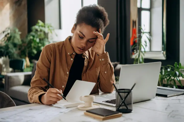 A black woman with head bowed, hand supporting the side of her head, in deep thought.