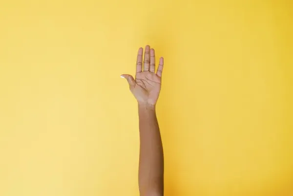 Raised hand against a yellow background.