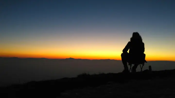 Man sitting on a camping chair watching the sunset glow on the horizon.