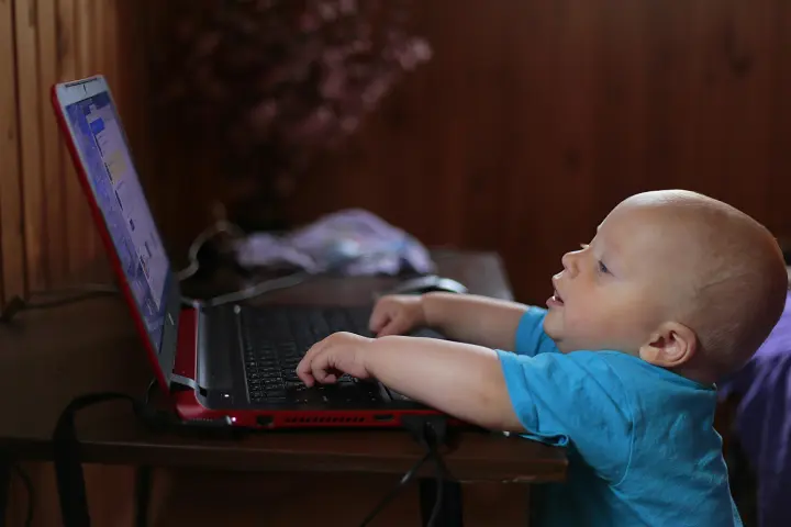 A baby is touching the keys of a laptop sitting on a small table.
