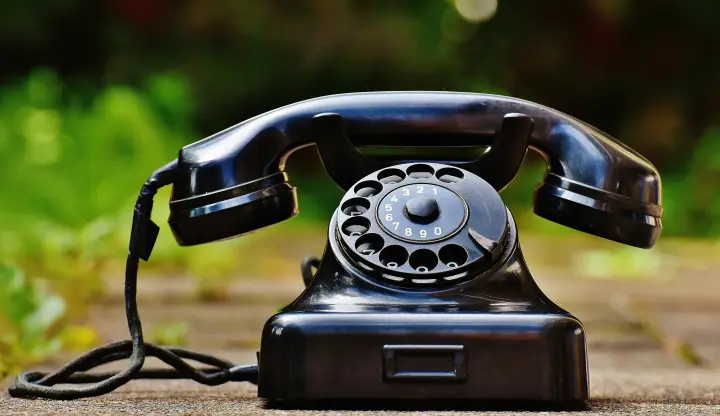 Old black rotary phone against an outdoor background.