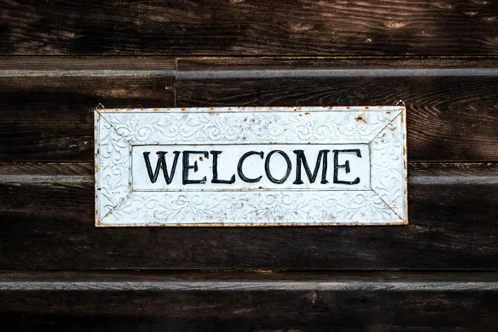 Welcome sign hung on a dark-colored wood wall.