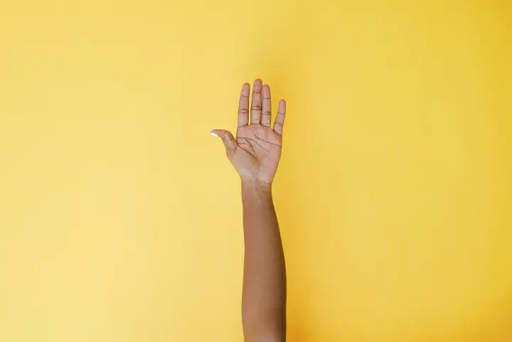 Raised hand against a yellow background.