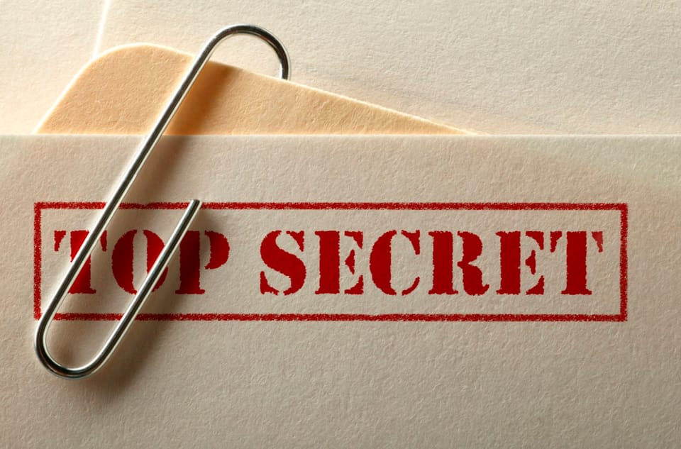 The top of a document with only "TOP SECRET" visible is paper clipped to the corner of a manila folder.